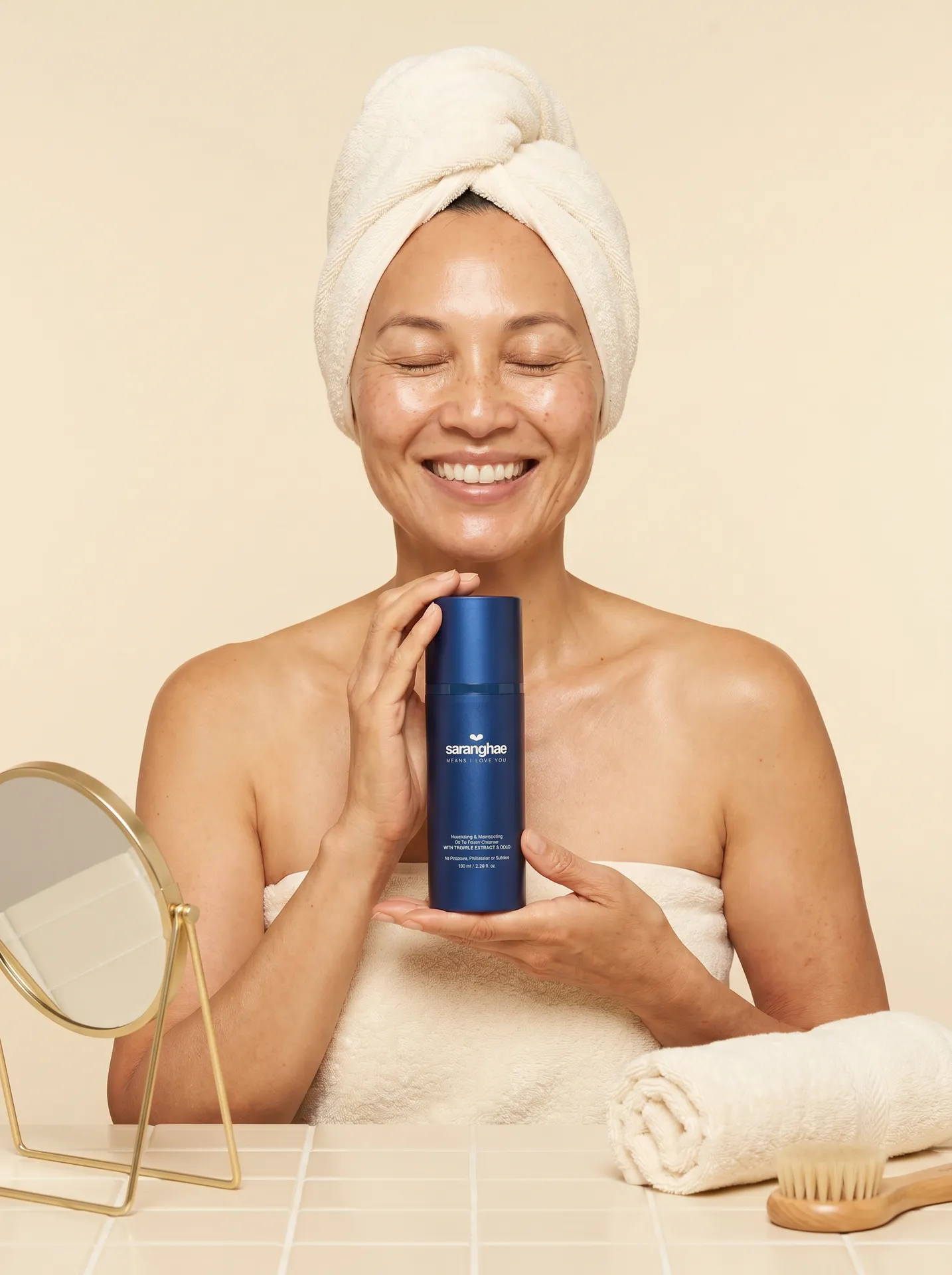 Woman with hair wrapped in a towel smiling while holding the Saranghae Oil + Foam Cleanser